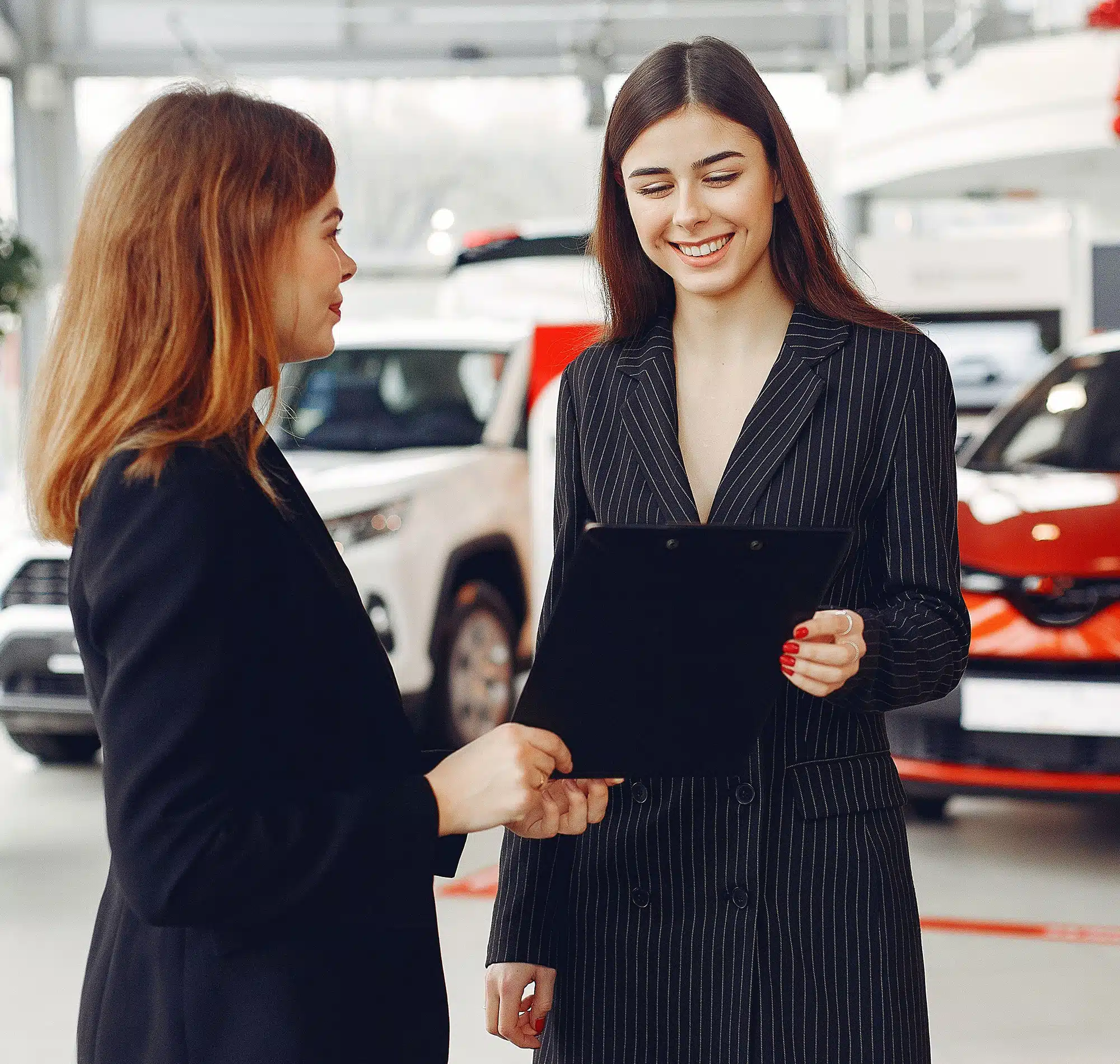 Two women smiling while reading documents at a car dealership.